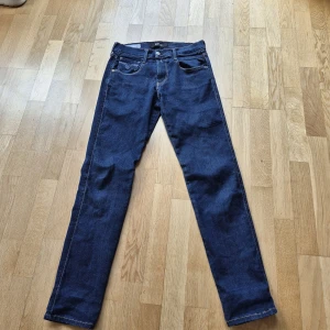 Mörkblå jeans från Replay - Säljer ett par mörkblå jeans från Replay med klassisk femficksmodell och raka ben. Jeansen har kontrastsömmar och detaljerade bakfickor med Replay- logga på linningen. Perfekta för en stilren och enkel look.