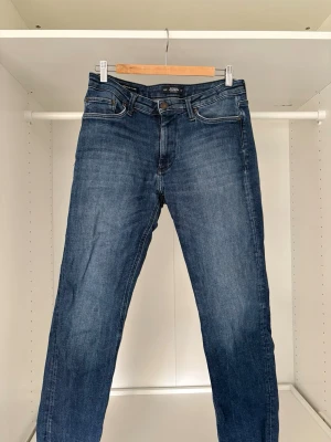Blå raka jeans från Jack&jones - Säljer ett par klassiska blå jeans från Jack&Jones med rak passform och fem fickor. Jeansen har en snygg tvättad look och är gjorda i denim med kontrastsömmar. Perfekta till en avslappnad stil och funkar året runt.