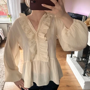 NY Krämvit blus med volanger - . Helt ny blus med volanger och med tag kvar. Storlek 34/36. 💕  OBS såg nu att den har en pytteliten fläck på framsidan, syns på bild 3, vid knapparna ungefär, som endast syns om man lyser med ficklampa, tror nog det går bort i tvätten men eftersom lappen är kvar vill jag ej tvätta den 💕   