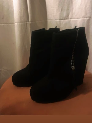 Svarta stövletter med dragkedja - Snygga svarta stövletter i mockaimitation med hög klack och dragkedja på sidan. Klassisk och stilren design som passar till många outfits. Perfekta för dig som vill ha en edgy look.