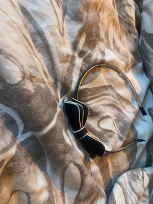 Svart diadem med rosett och vita kanter - Snyggt svart diadem med en stor rosett på sidan, dekorerad med vita kanter för en kontrastfull look. Diademet är smalt och har mjuka ändar för extra komfort. Perfekt accessoar för att lyfta din outfit med en söt detalj.