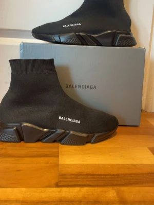 Strumpskor Speed Trainer svarta sneakers - Svarta Strumpskor Speed Trainer sneakers med stickad ovandel i textil och vit logga på sidan. Skorna har en strumpliknande passform och chunky svart sula med grafiska detaljer. Perfekta för dig som gillar en modern och sportig look.