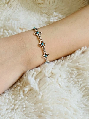 Silverarmband med turkosa pärlor - Snyggt armband i silverfärg med blommiga länkar där varje blomma har en liten turkos pärla i mitten. Armbandet har ett smidigt lås och ger en bohemisk och unik vibe. Perfekt för dig som gillar detaljer och färg.