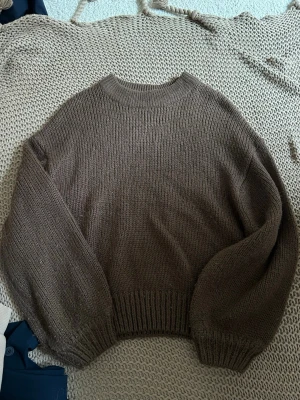 Brun stickad tröja från NA-KD - Mysig brun stickad tröja från NA-KD med rund halsringning och långa ärmar. Tröjan har ribbade muddar vid ärmslut och nederkant, vilket ger en snygg och avslappnad passform. Perfekt för lager på lager under kyliga dagar.