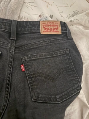 Svarta bootcut jeans från Levi's - Säljer ett par svarta bootcut jeans från Levi's med klassisk femficksdesign och röd Levi's-tag på bakfickan. Jeansen har en något utsvängd passform och är tillverkade i slitstark denim. Perfekta för en avslappnad och trendig look. Köpa på Levis hemsida storlek: midja 25 längd 30. De är svarta men blivit lite lite gråa i tvätten annars är de jätte fina.