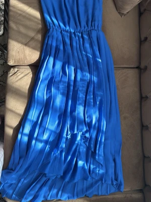 Blå plisserad långklänning - Snygg blå långklänning med markerad midja. Klänningen är ärmlös och har en elegant, flytande siluett som ger en lyxig känsla. Perfekt för dig som vill sticka ut med en färgstark look. Funkar perfekt både för fest och en solig sommardag. Anledning till att jag säljer är på grund av att det inte är min stil. 