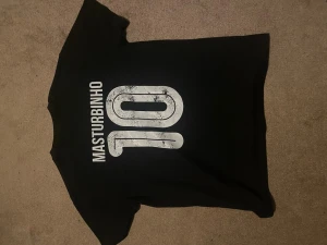 Svart t-shirt med tryck och nummer - Cool svart t-shirt med stort vitt tryck på ryggen där det står 'MASTURBINHO' och siffran 10. Klassisk passform med korta ärmar och rund hals. Perfekt för dig som gillar unika och sköna plagg med sportig vibe.