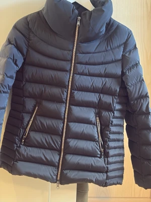 Svart pufferjacka från Colmar - Snygg svart pufferjacka från Colmar med hög krage och två dragkedjeförsedda fickor framtill. Jackan har quiltad design och Colmar-logga på ärmen. Perfekt för kalla dagar och riktigt skön att bära. Materialet är lätt och isolerande.