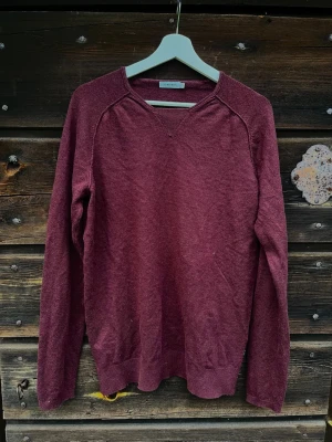 Vinröd J.Lindeberg Tröja - Vinröd långärmad tröja från J.Lindeberg med ribbade muddar. Tillverkad i ull, enkel och stilren design utan tryck eller mönster.