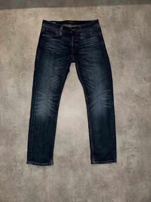 Mörkblå jeans från Jack & Jones - Säljer ett par mörkblå jeans från Jack & Jones med snygga slitningar och klassisk femficksmodell. Jeansen har raka ben och kontrastsömmar, perfekta till vardagslooken. Tillverkade i bomull med lite stretch för extra komfort. Hör av vid minsta fundering