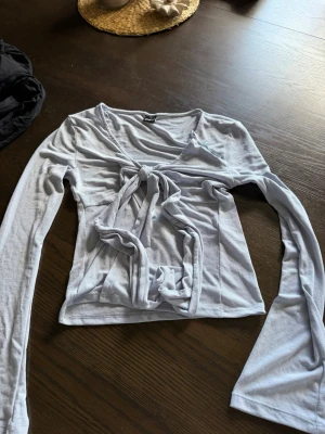 Ljusblå omlottopp med knyt - Trendig ljusblå omlottopp från Gina Tricot med långa ärmar och v-ringning. Toppen har knyt framtill som ger en snygg och justerbar passform. Perfekt att styla med jeans eller kjol för en cool look.