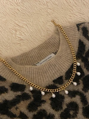 Guldfärgat halsband med pärlor - Snyggt halsband i guldfärgad rostfritt med kedja och hängande vita pärlor. Kedjan har en klassisk, chunky design och pärlorna ger en trendig och elegant touch. Perfekt accessoar för att lyfta din outfit.