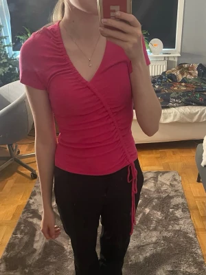 Rosa topp med snörning - Säljer en rosa topp från mango med snörning längs sidan och v-ringad hals. Toppen är kortärmad och har en slim passform som framhäver figuren. Ny utan prislapp 