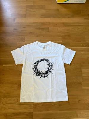 Vit t-shirt med svart grafiskt tryck - Vit t-shirt med ett stort svart grafiskt tryck av en taggig krans på bröstet. Klassisk passform och rund halsringning, perfekt för en stilren och edgy look.