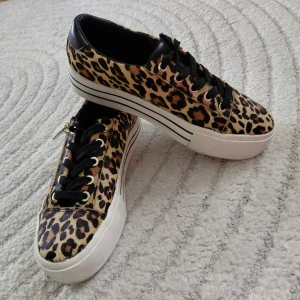 Leopardmönstrade sneakers med platåsula, Stradivarius, 37 - Snygga sneakers med leopardmönster och svart läderdetalj vid hälen. Skorna har svart snörning, vita platåsulor med svarta ränder och cool streetstil. Perfekta för dig som vill sticka ut med ett djurmönstrat statement. Innermått 24cm. Knappt använd.