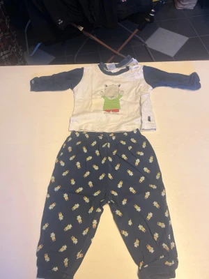 Blå och vit pyjamas med djurmotiv - Söt tvådelad pyjamas med långärmad tröja i vitt och blått med ett gulligt djurmotiv på bröstet. Byxorna är blå med små djurtryck över hela tyget och har resår i midjan. Perfekt för mysiga kvällar hemma.