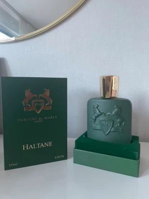 Parfums de Marly Haltane 125ml - Lyxig parfym från Parfums de Marly, modellen Haltane. Flaskan är matt grön med guldfärgat lock och har en elegant relief med två hästar och logotypen 1743. Kommer i en snygg grön förpackning med gulddetaljer. Perfekt för dig som gillar exklusiva dofter.