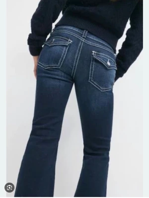 Mörkblå bootcut jeans Gina tricot  - Snygga mörkblå bootcut jeans med vita kontrastsömmar och fickor med lock och knapp bak. Jeansen har låg midja och är helt nya från Gina tricot. Dem är storlek 158 precis som Xs