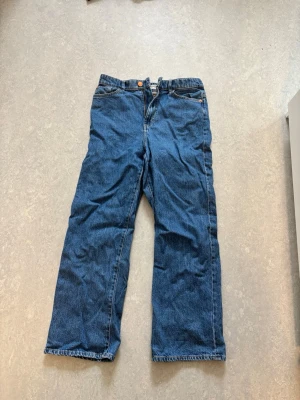 Blå raka jeans med normal passform - Klassiska blå jeans med raka ben och normal passform. Jeansen har fickor, knappgylf och är tillverkade i ett slitstarkt bomullstyg. Perfekta för en avslappnad och tidlös stil. Säljer då de tyvärr blivit för små för mig. 