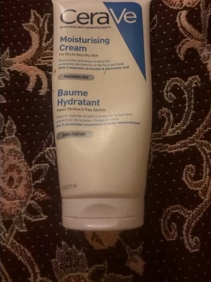 CeraVe Moisturising Cream - CeraVe Moisturising Cream är en vit, parfymfri kräm för torr till mycket torr hud. Innehåller 3 essentiella ceramider och hyaluronsyra som återfuktar och stärker hudens skyddsbarriär. Tuben är vit med blå detaljer och text. Mer än hälften kvar 
