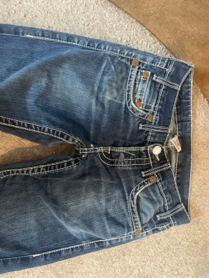 Lowwaist True Religion jeans!!!! - Jätte snygga och bekväma trueys!! Sitter lowwaist straight/bootcut på mig (bild 5 visar) och och super fina o bekväma!!! Säljer då dem inte kommer till användning men har varit mina favorit byxor!!! OBS!!!: varför dem är billigare än vanligt är pga av att när jag köpte dem så var de hål mellan bena på dem men jag har lagat dem hos en skräddare så nu e dem hela!! Plus att när du har på dig dem så syns det inte att det varit hål utan ser ut o va i toppenskick!!! (Kolla bild 6 för att se hålet)😱❤️❤️❤️