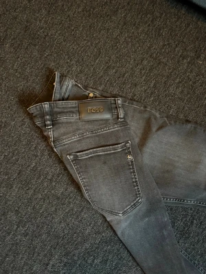 svarta  jeans från BOSS - Snygga mörkgrå jeans från BOSS med klassisk femficksmodell och diskret tvättad look. Jeansen har raka ben och en stilren läderpatch med BOSS-logga bak i midjan. Perfekta för dig som gillar en clean och modern stil.
