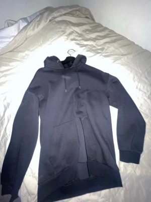 Svart hoodie från Pier One - Klassisk svart hoodie från Pier One med huva och dragsnören. Hoodien har en stor magficka och ribbade muddar vid ärmar och nederkant. Tillverkad i mjukt bomullsmaterial som känns skönt mot huden. Perfekt för en avslappnad och stilren look.