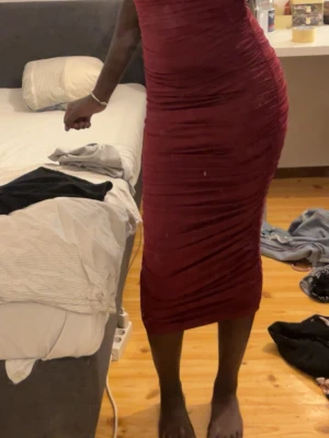 Vinröd tight långklänning - Säljer en vinröd långklänning med tight passform och rynkade detaljer längs hela klänningen. Klänningen är ärmlös och har en kroppsnära siluett som framhäver formerna. Perfekt för dig som vill sticka ut med en elegant look.