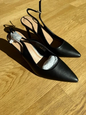 Svarta slingback pumps med spetsig tå - Stilrena svarta pumps med spetsig tå och smal klack. Skorna har öppen häl med justerbar rem och spänne. Helt oanvända🩷Perfekta för en utekväll eller för att lyfta en tråkig vardagsoutfit🤩 
