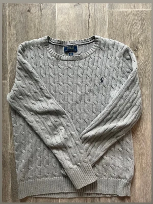 Grå kabelstickad tröja Polo Ralph Lauren - Kabelstickad grå tröja från Polo Ralph Lauren med rund halsringning, står xl men det är barn storlek så den passar den längden 170-180.              Nypris 1300