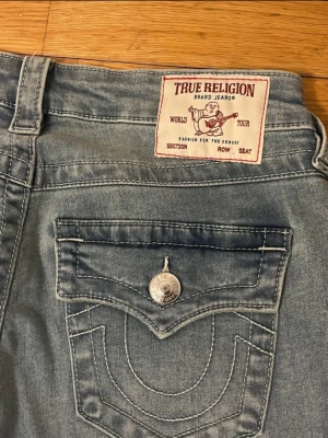 Ljusblå bootcut jeans True Religion - Snygga ljusblå bootcut jeans från True Religion med klassiska kontrastsömmar och ikoniska fickdetaljer bak. Jeansen har hög midja och silverfärgade knappar. Perfekta för dig som vill ha en trendig och avslappnad look.