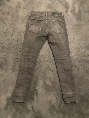 Grå slim jeans från G-Star RAW - Säljer ett par grå slim fit jeans från G-Star RAW med snygga slitningar. Materialet är mjukt och stretchigt. Storleken är W30 och L32