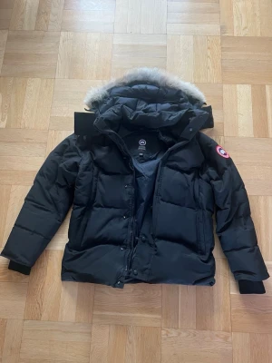 Canada Goose Wyndham parka - M  - Säljer en svart dunjacka från Canada Goose med pälskantad huva och klassisk logga på ärmen. Jackan har dragkedja och knappar framtill, samt flera fickor. Perfekt för kalla vinterdagar tack vare det tjocka dunfodret och den höga kragen.en jacka som garanterat håller dig varm, lite för varm enligt mig själv.  In köpt på jonells vintern 24 för 18.990kr 