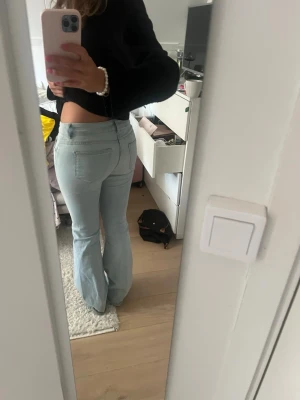 Ljusblå utsvängda jeans - Säljer ett par ljusblå jeans med utsvängda ben och hög midja. Jeansen har klassiska bakfickor och är i en mjuk denim som sitter snyggt på kroppen. Perfekta för dig som gillar retrostil och vill ha ett par trendiga jeans i garderoben.