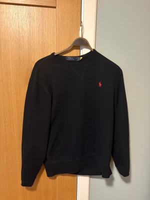 Svart sweatshirt från Polo Ralph Lauren - Klassisk svart sweatshirt från Polo Ralph Lauren med rund halsringning och röd broderad logga på bröstet. 