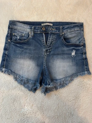 Jeansshorts  - Säljer dessa blå jeansshorts från Place du Jour med fransig kant och slitna detaljer 💖💖💖