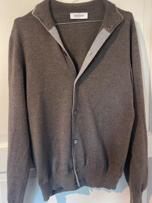 Gran Sasso kofta - Klassisk brun kofta från Gran Sasso i mjukt och tunt stickat material. Koftan har knäppning framtill, ribbade muddar vid ärmslut och nederkant samt en enkel, stilren design. Perfekt för lager-på-lager och passar till många olika outfits.