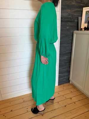 Grön långklänning med knappar - Använd en gång: Stilren grön långklänning med knappar framtill och resår i midjan. Klänningen har långärmade ärmar med lätt puff och avslappnad passform. Perfekt för dig som vill ha en enkel men snygg look. Storlek 38 , passar även 36 också. 