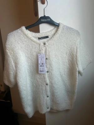 Vit kortärmad kofta från Ginatricot - Jätte mjuk fluffig T-shirt från Gina tricot som man skulle kunna ha både stängd och öppen då kan även kan användas som en kofta, en extra knapp tillkommer. Tröjan är nyskick och aldrig använd😊 (nypris 399) 
