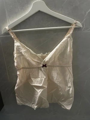 Odd Molly spetsdetaljerad linnetopp - Supersöt ljusbeige linnetopp från Odd Molly med spetsdetaljer och liten rosett framtill. Tunt och luftigt material, perfekt för varma dagar. V-ringad och med smala axelband.