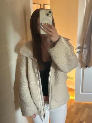 Beige teddyjacka med dragkedja - Mysig och oversized teddyjacka i beige med stor krage och dragkedja framtill. Jackan har en fluffig och mjuk känsla, perfekt för kyliga dagar. Passar dig som gillar en avslappnad och trendig stil. Ända lilla bekymmret är att inuti jackan längst ned så är den lite avfärgad av ett par svarta jeans vilket man ser på bilden 