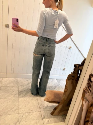 Ljusblå raka jeans med slitningar - Säljer ett par ljusblå jeans med raka ben och coola slitningar på knä och lår. Jeansen har klassisk femficksdesign och låg midja. Perfekta för en avslappnad och trendig look.