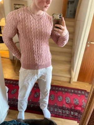 Rosa kabelstickad tröja Morris - Säljer en rosa kabelstickad tröja från Morris med broderad logga framtill. Tröjan har rund halsringning, ribbade muddar och är tillverkad i mjukt material. Perfekt för dig som gillar klassisk och stilren look.