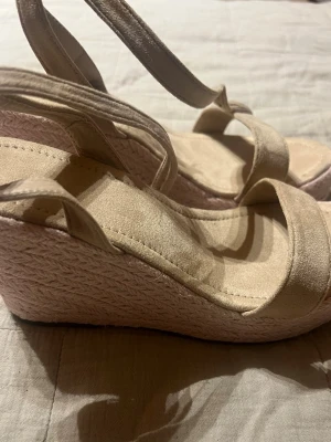 Beige espadrille sandaler med remmar - Använda 1 gång! Snygga beige sandaler med platåsula i espadrillestil och breda remmar över foten samt justerbara ankelband. Ovandelen är i mockaimitation och sulan har flätad detalj. Perfekta för sommaren och ger en avslappnad men trendig look.
