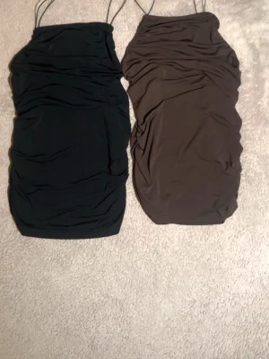 Svart och brun ruched toppar - Två snygga linnen med ruched detaljer och tunna axelband. Den ena är svart och den andra är brun, båda har en kroppsnära passform och är perfekta för att skapa en trendig look. Materialet känns mjukt och stretchigt.