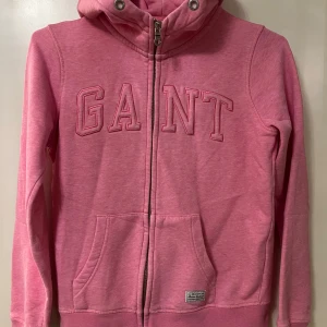 Rosa hoodie från GANT - Säljer en rosa hoodie från GANT med dragkedja och huva. Tröjan har fickor framtill och broderad logga på bröstet. 