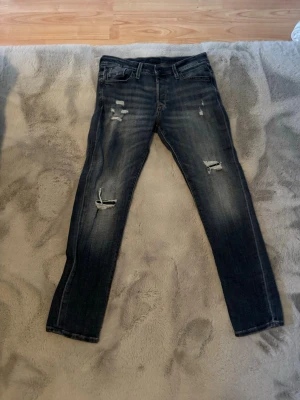 Mörkblå slitna skinny jeans från Jack and Jones  - Snygga mörkblå skinny jeans med slitningar och hål på benen. Jeansen har klassisk femficksdesign, dragkedjegylf och bälteshällor. Perfekta för en trendig och avslappnad stil.