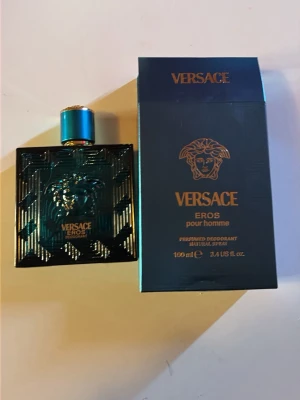 Versace Eros deodorant spray 100 ml -  Aldrig använt. versace Eros  i en lyxig turkosblå glasflaska med gulddetaljer och Medusa-huvud på framsidan. Flaskan har en elegant, fyrkantig form och matchande turkosblå förpackning med guldfärgad text. Volym: 100 ml.