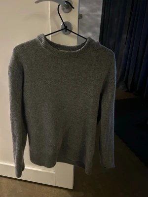 Grå stickad tröja i ullmix - Mysig grå stickad tröja med rund hals och långa ärmar. Tröjan har en enkel, klassisk design och är tillverkad i mjuk ullmix som håller dig varm. Perfekt för lager på lager och passar till det mesta i garderoben.