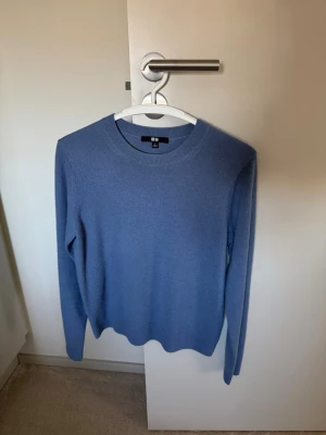 Blå stickad tröja från Uniqlo - Säljer en stilren blå stickad tröja från Uniqlo. Tröjan har rund halsringning, långa ärmar och ribbade muddar vid hals, ärmslut och nederkant. Perfekt för lager på lager och enkel att matcha med olika outfits.